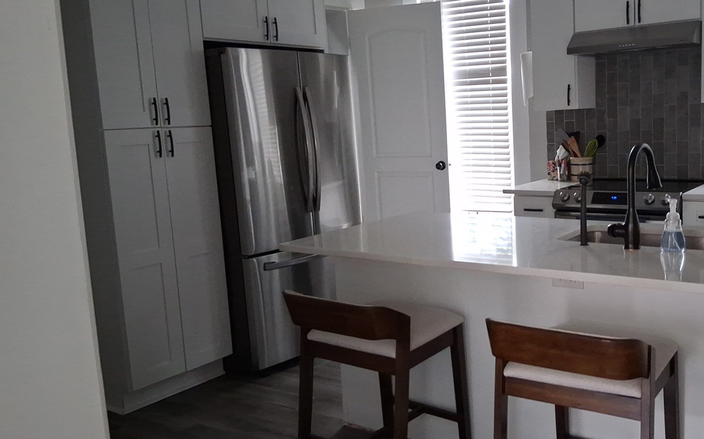 Kitchen reset after a turnover clean Short-term rental kitchen with white cabinets, stainless refrigerator and island seating after a turnover clean