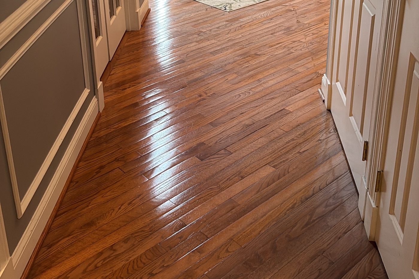 Hardwood floors after a house cleaning visit Polished hardwood hallway floor with white wainscoting and panelled doors after a cleaning visit