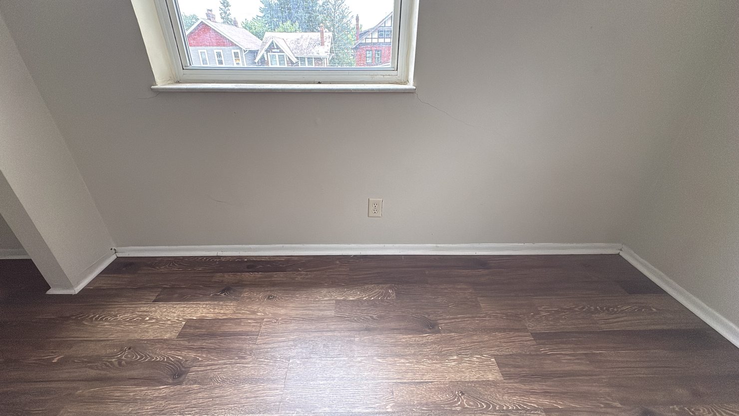 Empty room cleaned before move-in Empty room with a cleaned wood-look floor, white baseboards and a daylit window