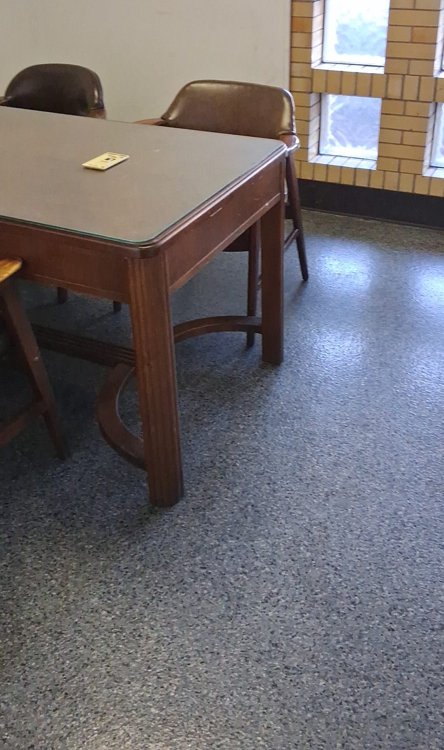 Common-area flooring in a workplace Common-area table and chairs beside daylit windows on a cleaned terrazzo floor